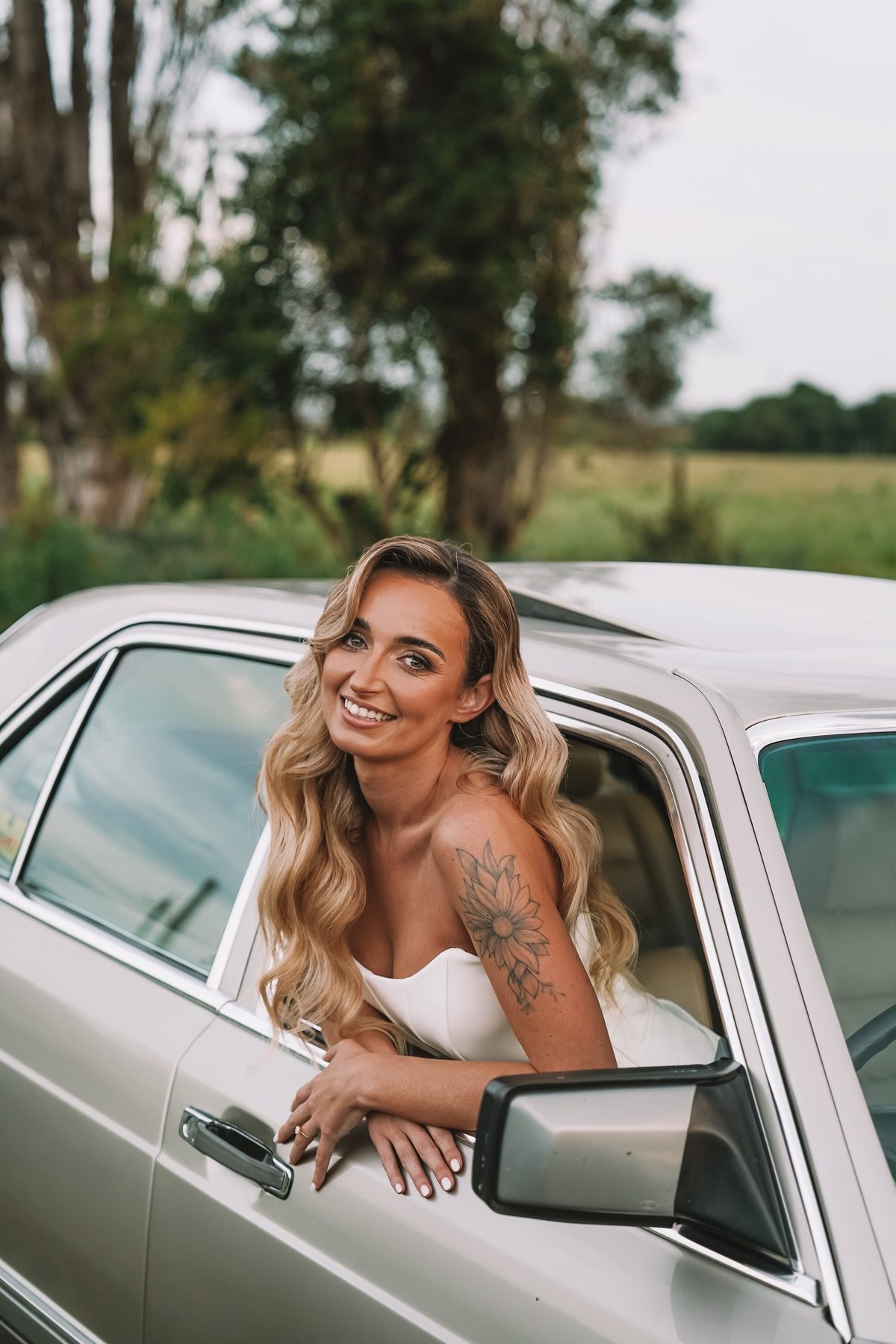 Bride leaning out of vintage car window, smiling