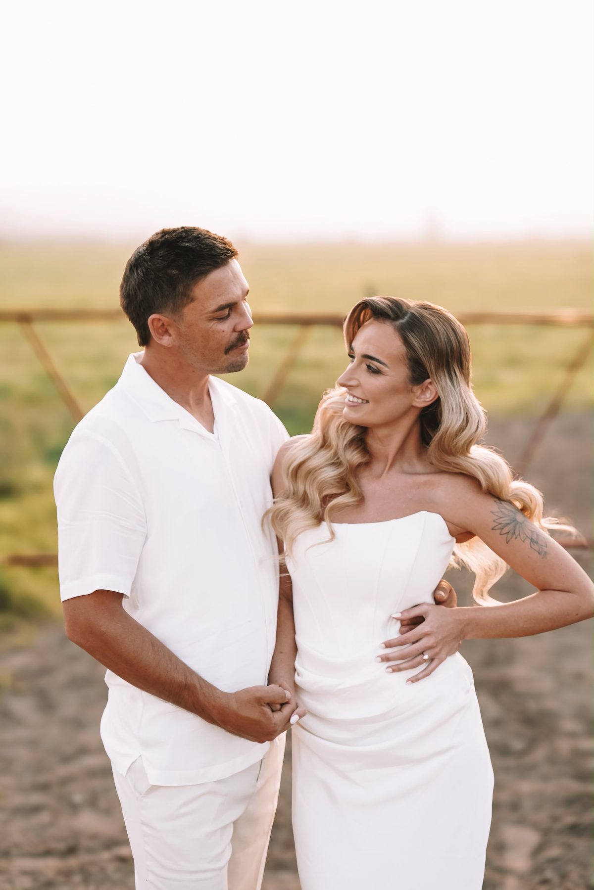Bride and groom in white, holding hands at sunset